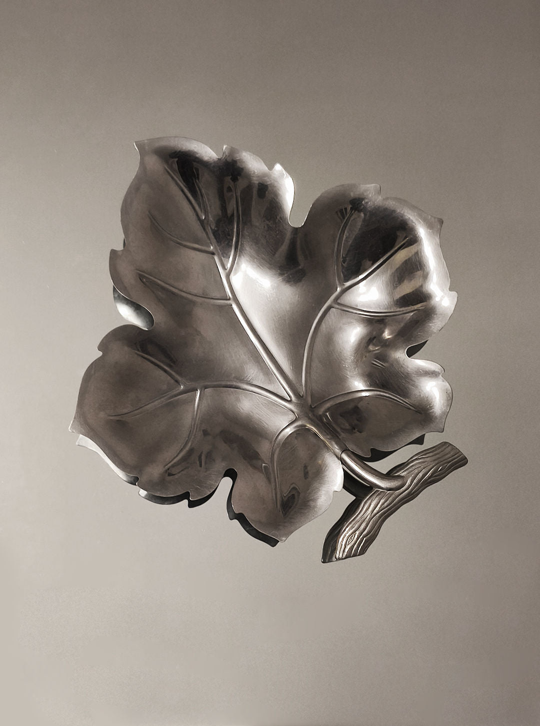 The Les Objoies Wine Leaf Vide-Poche is a polished stainless steel sculpture with a broad leaf design featuring prominent veins and a short stem. Its minimalist, glossy finish enhances the curves, reflecting light beautifully against a smooth, neutral background.