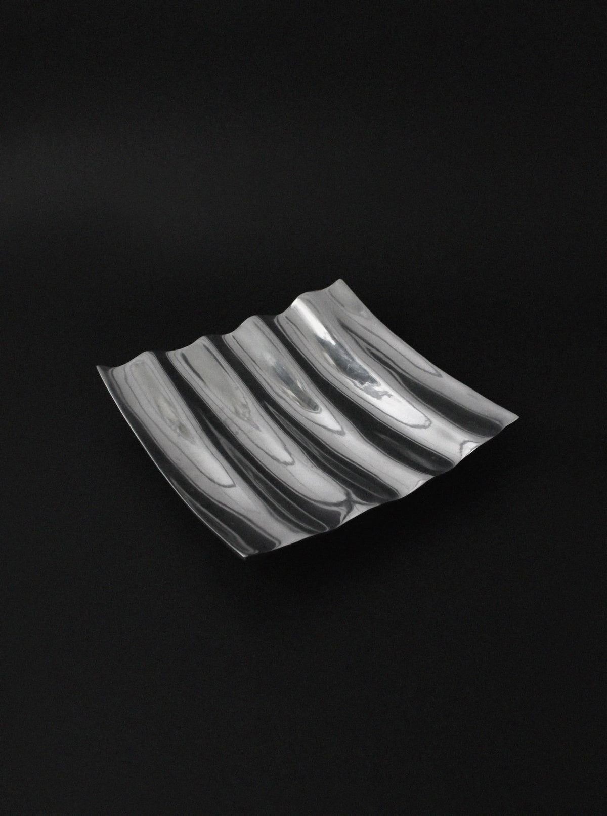 Polished aluminum wave bowl with curved ridges on black background