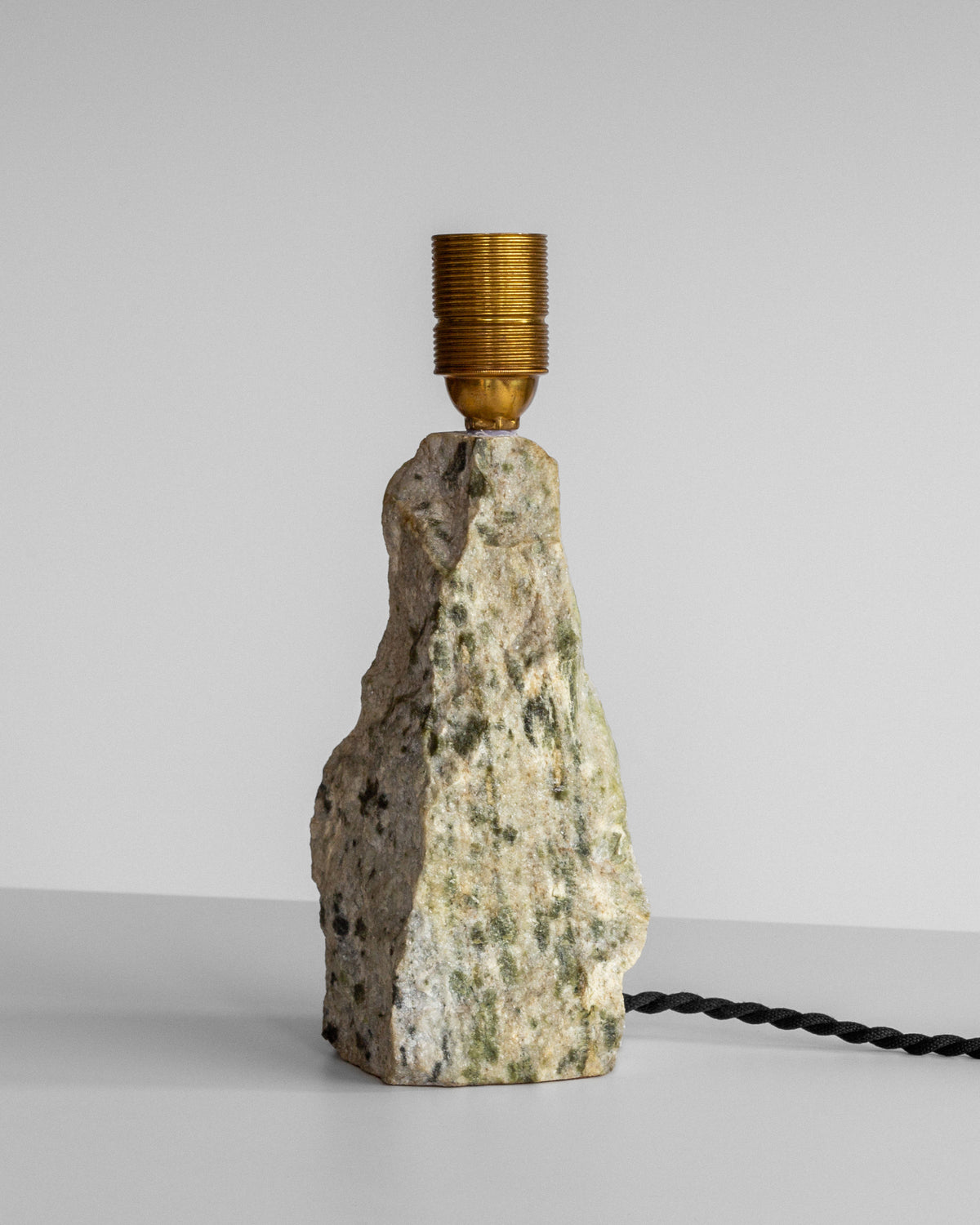 Introducing the Marble Stone Table Lamp by Spigel—an elegant minimalist lamp showcasing a Dunkeld marble base, complemented by a golden bulb socket and a twisted black cord, all set against a plain gray background.