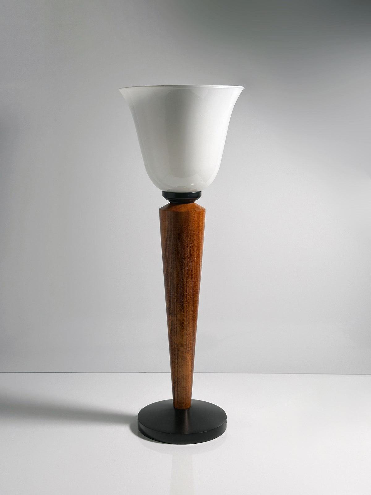 A Pair of Art Deco Chalices with frosted glass from Dodo Vintage elegantly tops tapered teak wood stems on black circular stands, set against a plain gray background.