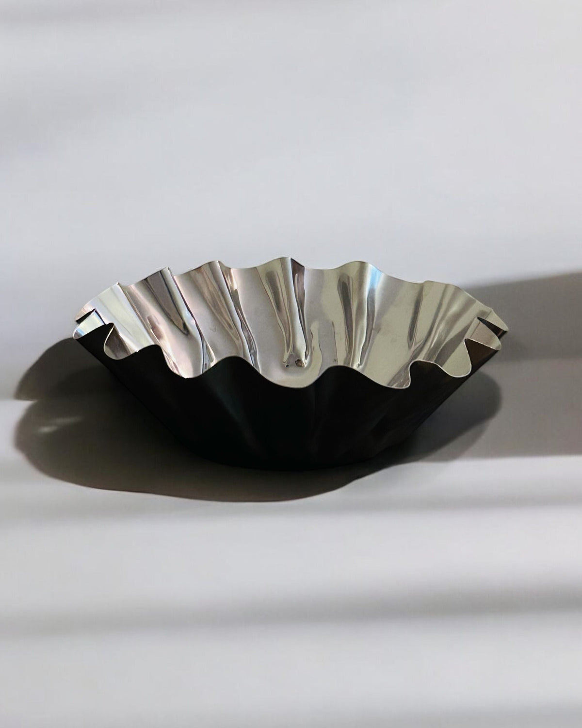 Wavy metallic bowl casting dramatic shadow on white surface