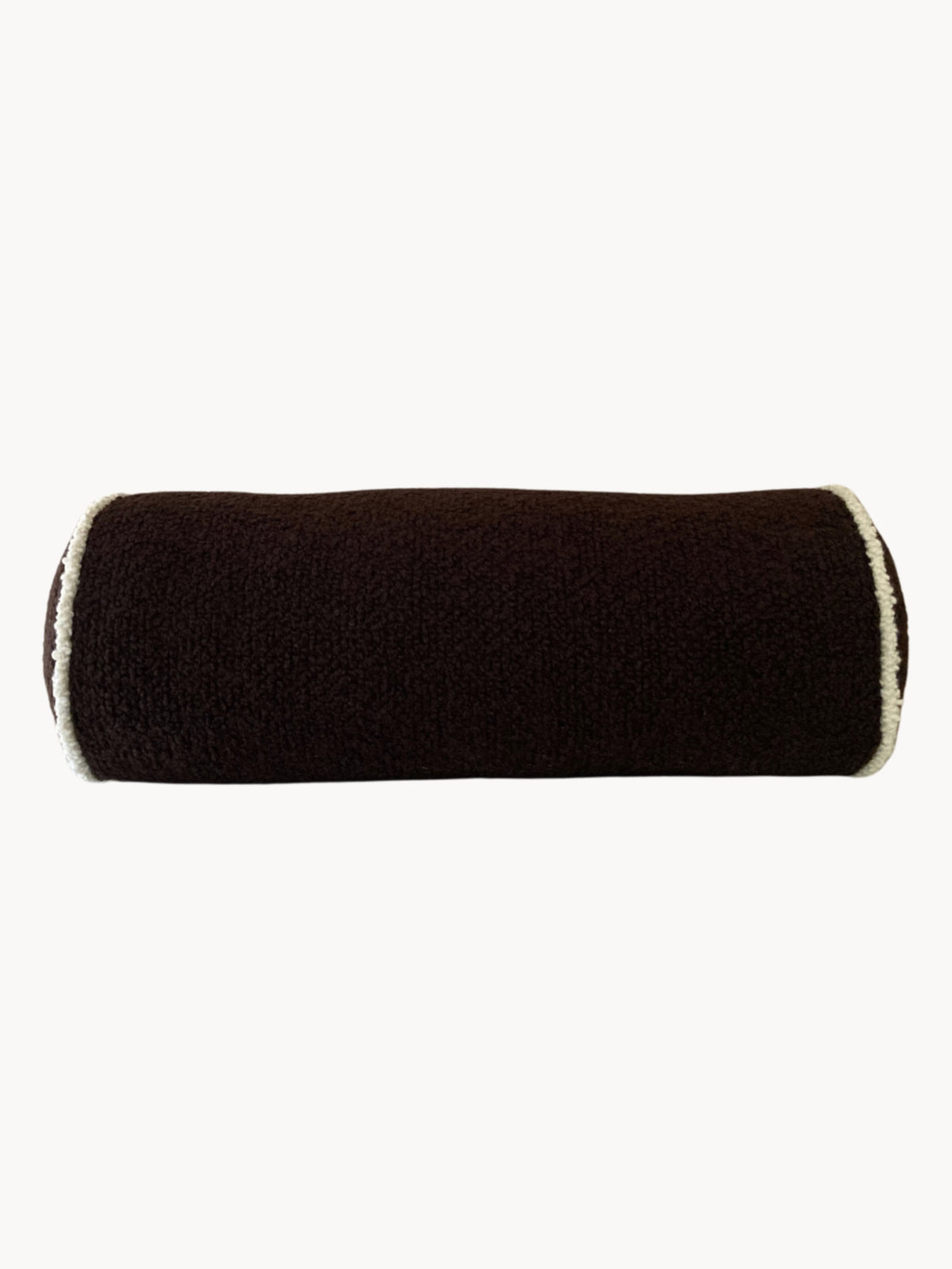 A cylindrical, black, bolster-style pillow with a soft, fuzzy texture made from luxurious wool bouclé fabric. The ends are adorned with a fuzzy white trim, providing a contrast to the dark fabric. Handmade in the UK, this plush and comfortable pillow is ideal for decorative or support use from AMÉLIORÉ—the "Le Cylindre - Passepoil - Wool Bouclé - Chocolate/Egg White.