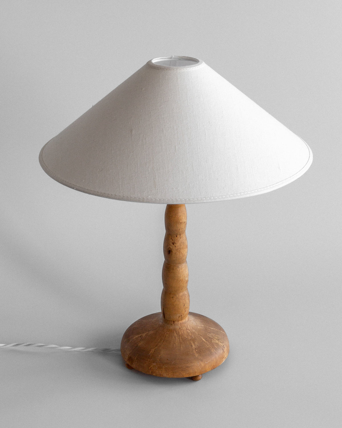 The Spigel Turned Birch Table Lamp, Sweden, features a round wooden base and turned birch stem with a large conical white shade. It sits on a neutral background with an elegant power cord extending from its base.