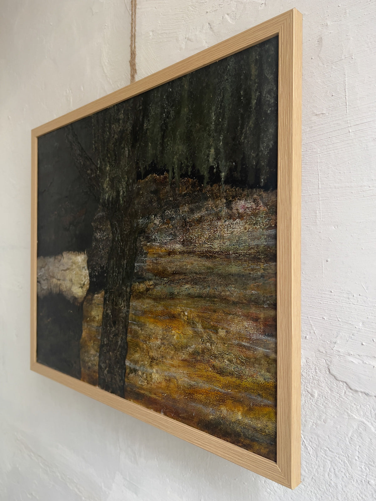 This side view shows the Veter Vintage "Vintage Landscape Painting, Oil on Canvas," depicting a dark tree against a textured earthy background. It hangs elegantly on a white wall, framed in light wood with visible string.