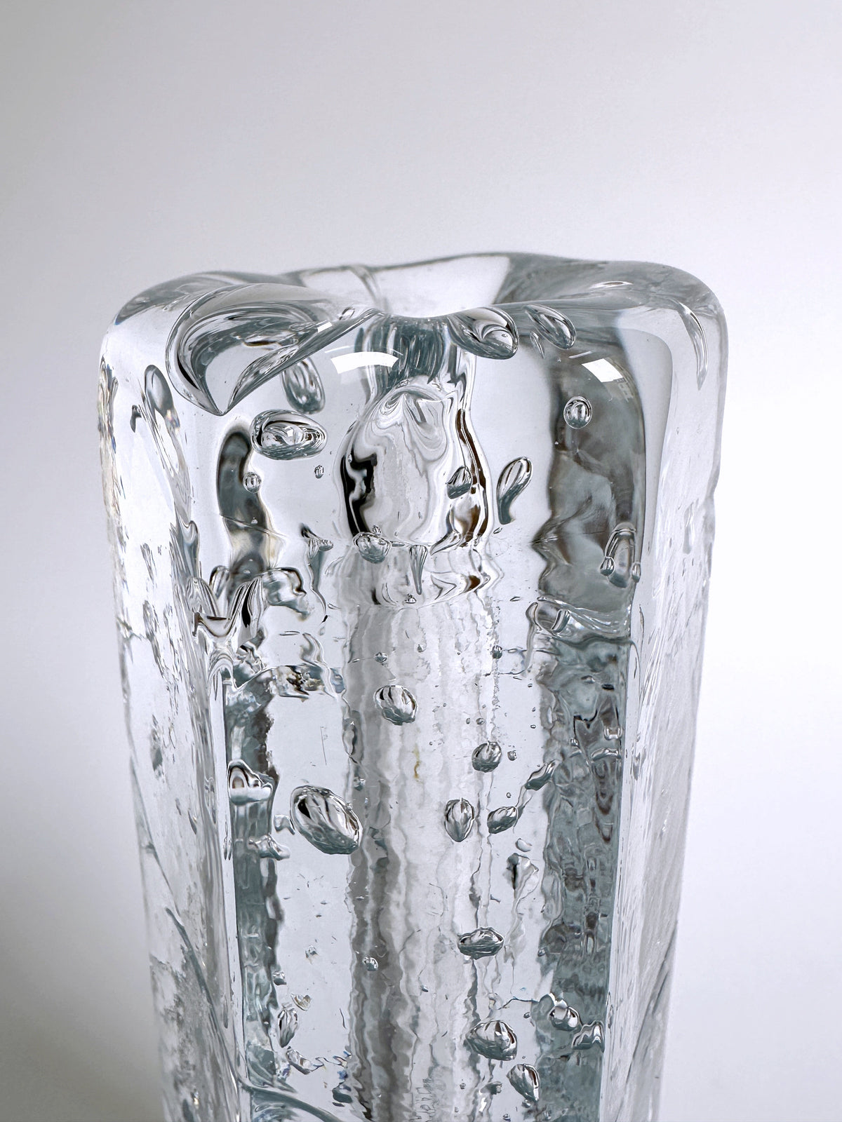 A close-up photograph of the 70s Swedish glass vase by Dodo Vintage, showcasing small air bubbles trapped within its thick glass walls. The Ice glass technique adds texture and visual interest to this vintage piece, set against a plain white background.