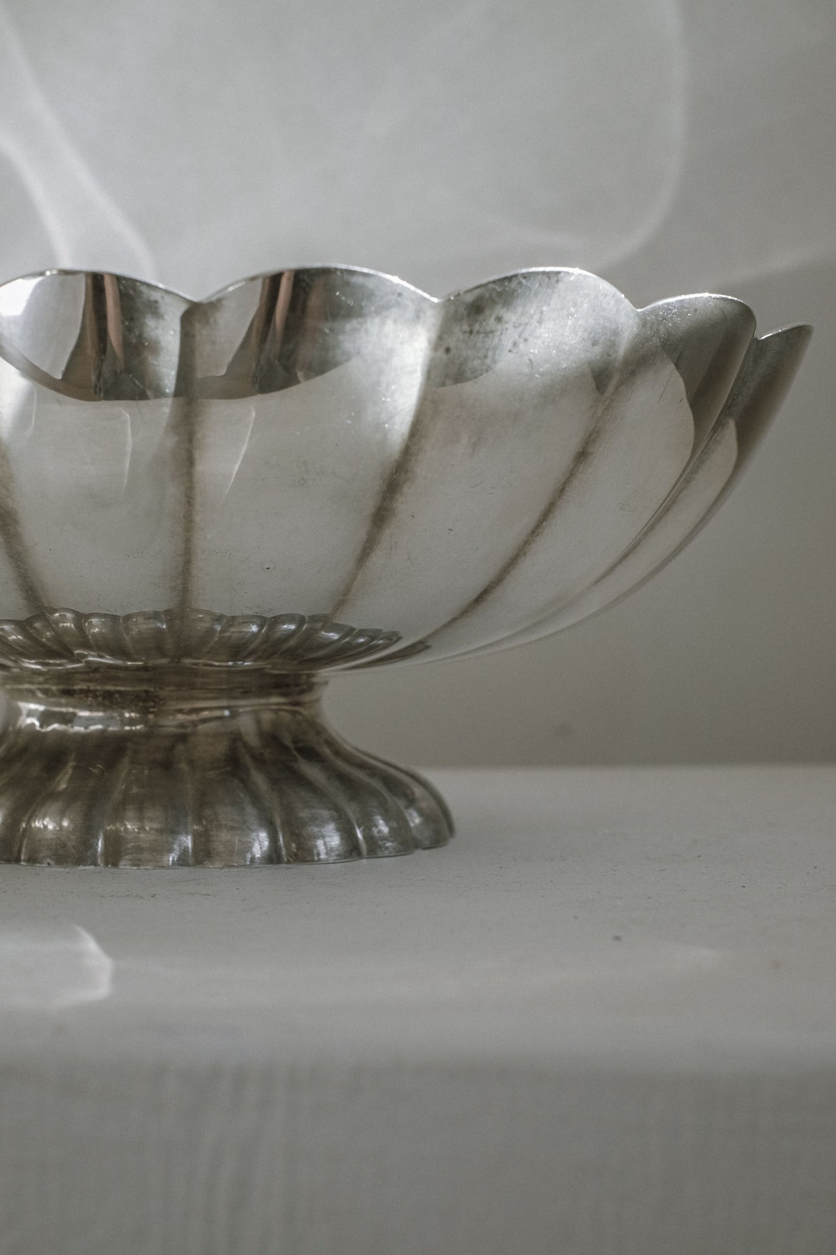 A close-up of the Silverplated Centerpiece by septembre studios featuring a scalloped edge and pedestal base, displayed on a white surface against a softly lit, neutral background.