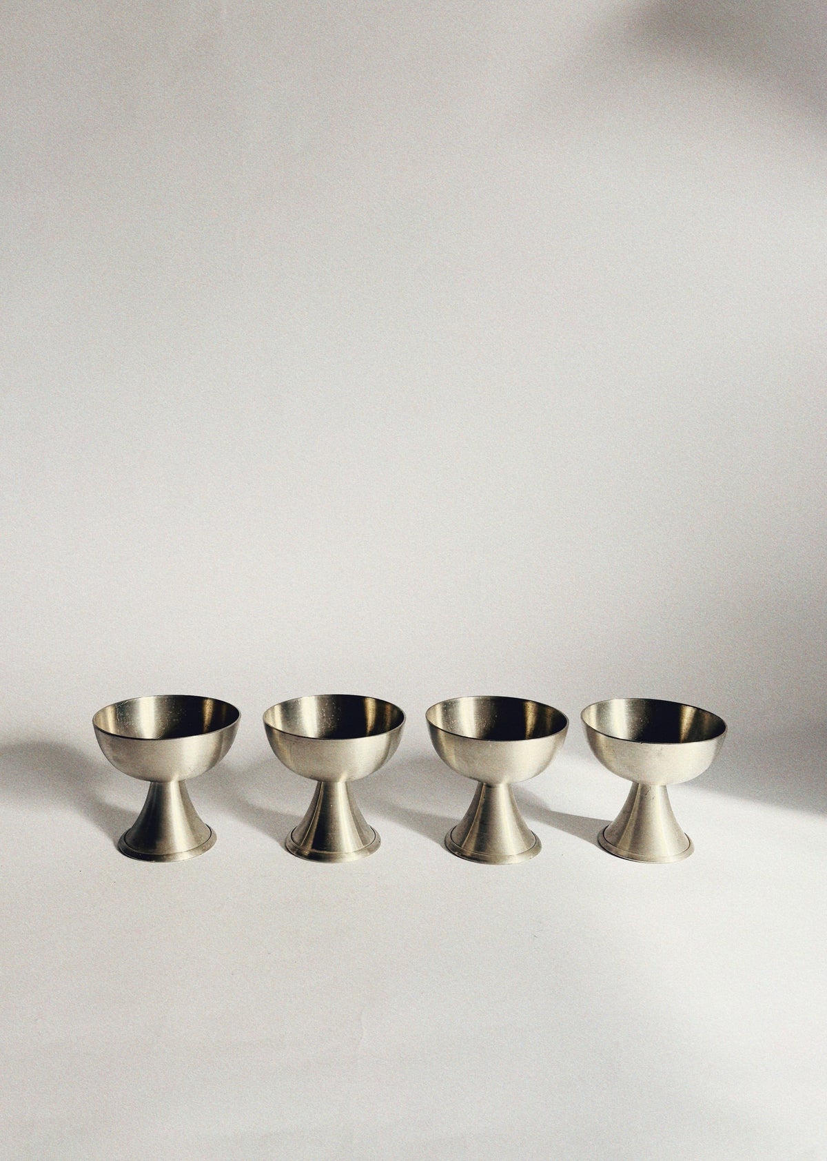 Set of four brushed brass dessert coupes on white surface