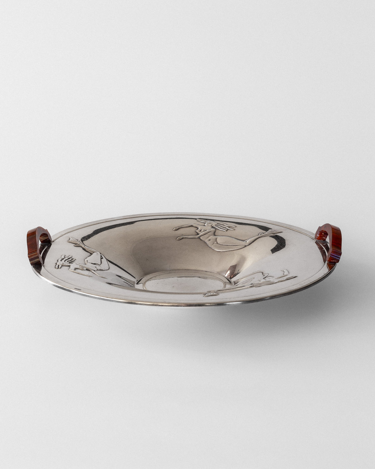 A 1930s Swedish silver-plated dish by Spigel with engraved deer and bird designs, featuring two curved Bakelite handles on opposite sides. The dish has a dark, glossy finish and a plain white background that highlights its elegant simplicity.