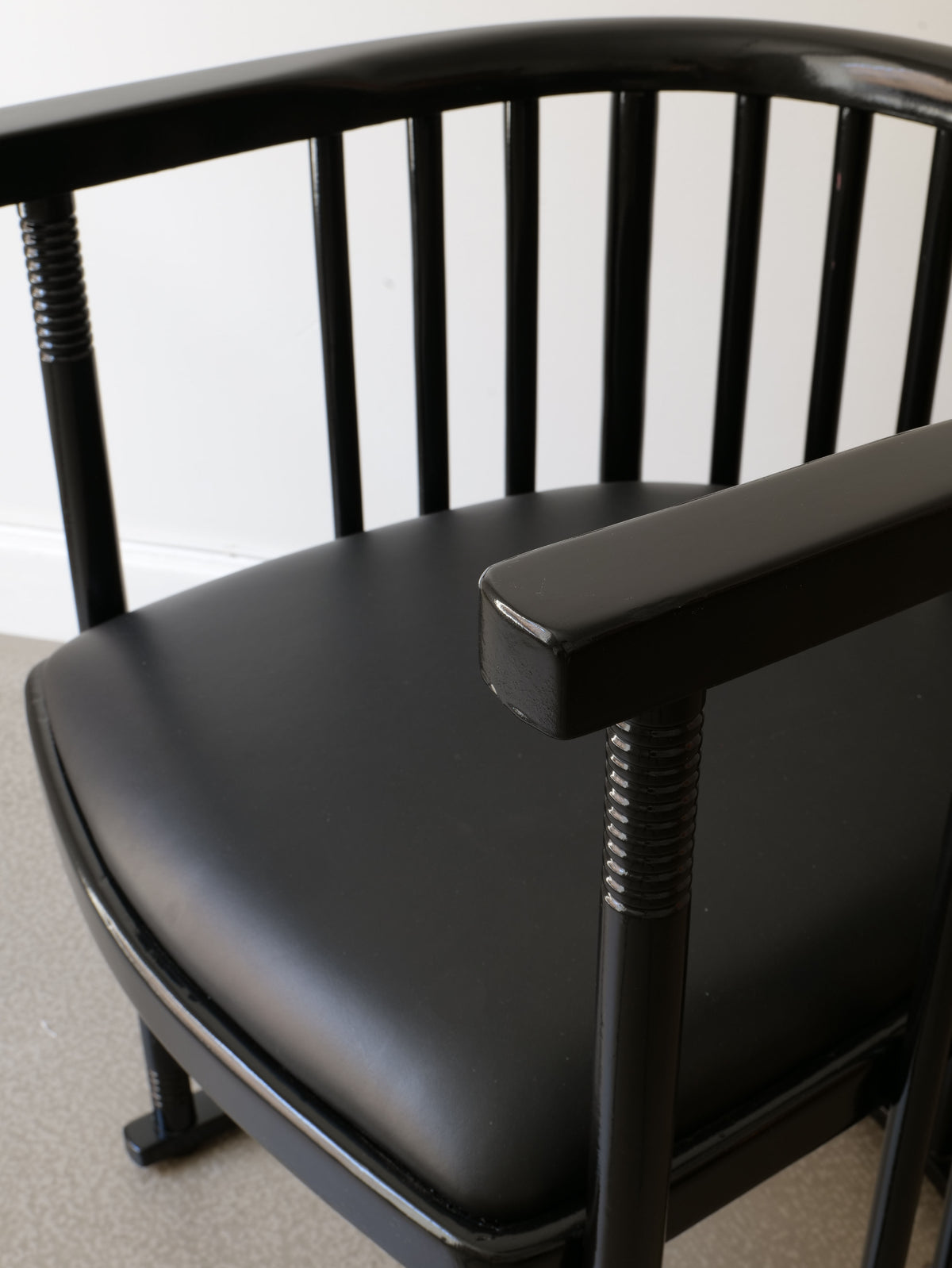 Placed against a light gray floor and white wall, the Bentwood Armchair Josef Hoffman from Collection apart offers a stylish touch to any room. This black wooden chair features a curved backrest and smooth seat, reminiscent of classic Josef Hoffman armchairs, with vertical slats along the backrest adding to its elegance.