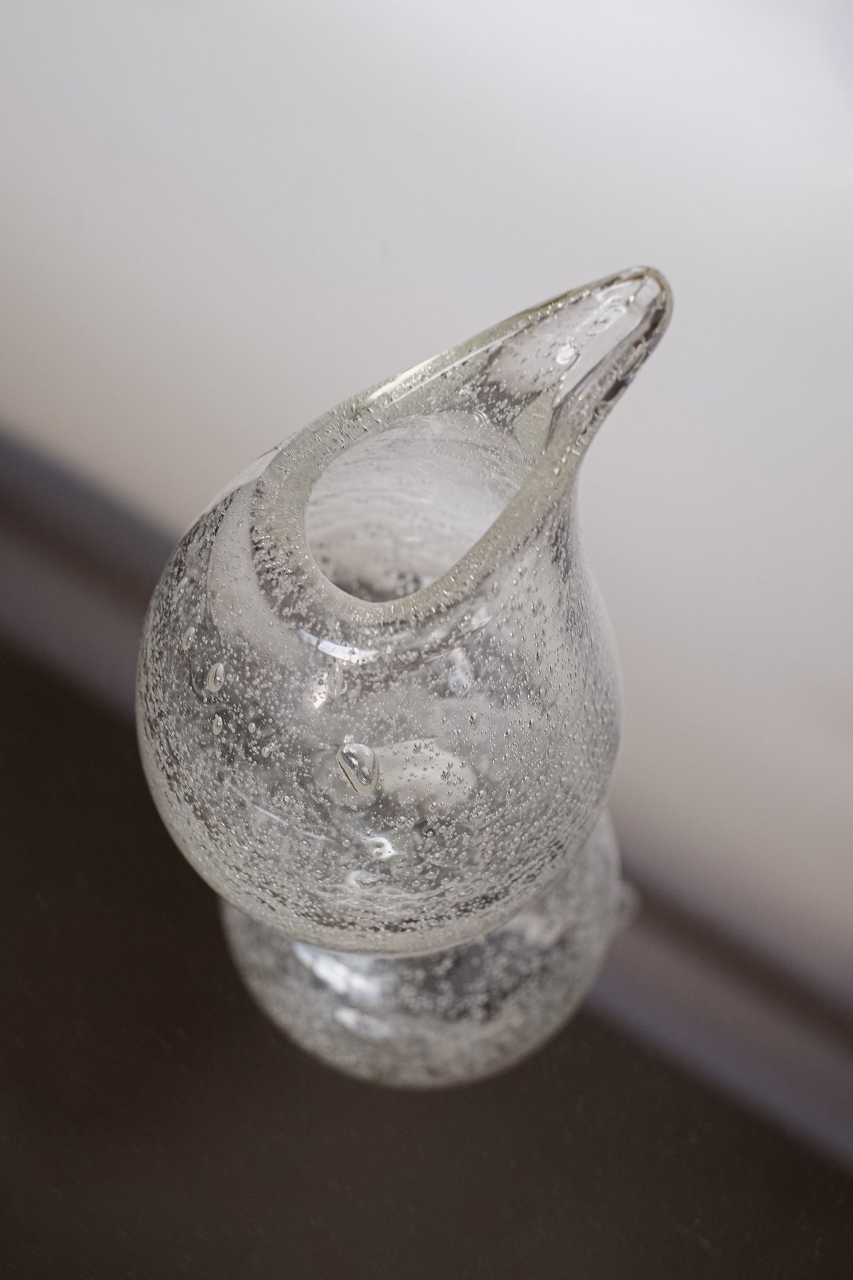 The Small Bubble Vase by septembre studios is a handmade glass vase with a unique curved teardrop shape, accented by textured bubbles. Its reflection shimmers beautifully on a dark, glossy background.