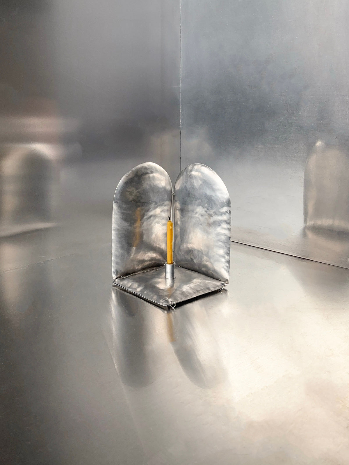 The Phaedra candle holder ALTAR by Bregje Sliepenbeek is a sleek, minimalist metal menorah with two curved panels and a beeswax candle in the center. Hand-made in Amsterdam, it creates an industrial, modern ambiance with its soft reflections.