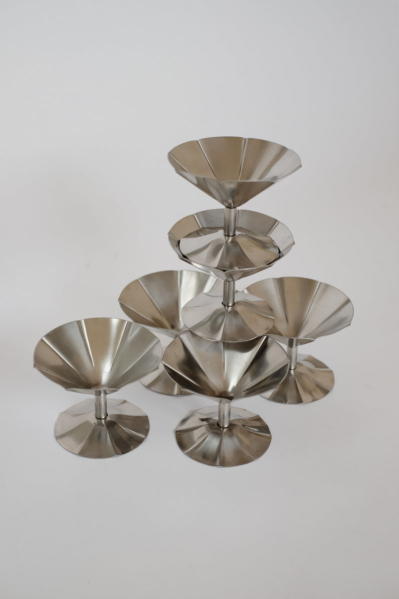 A pyramid of septembre studios' Set of 6 Ice Coupes, crafted in polished stainless steel, stands against a neutral backdrop. The reflective surface highlights the modern minimalist aesthetic.