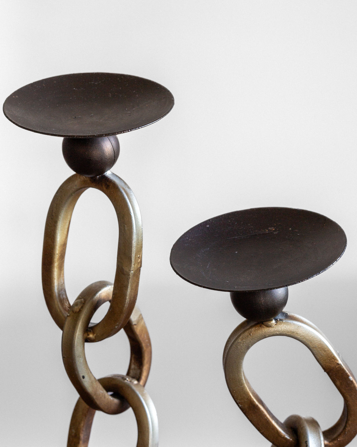 The Postmodern Sculpture Duo by Spigel includes two metal candle holders with a unique design featuring interlinked oval loops. Each holder is topped with a circular flat top to hold a candle. The rustic, textured finish of the loops imparts an industrial yet artistic aesthetic, making these candle holders ideal for aficionados of postmodern metal sculptures and enthusiasts of industrial decor.