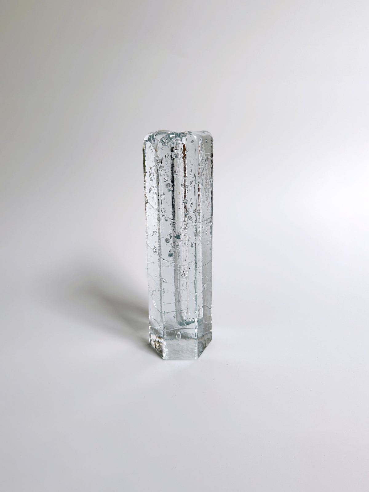 A rectangular, transparent glass vase by Dodo Vintage stands upright against a light gray background. Created using the Ice Glass technique popularized by Pukeberg Sverige, its slightly textured surface and air bubbles within add to its abstract and artistic appearance.