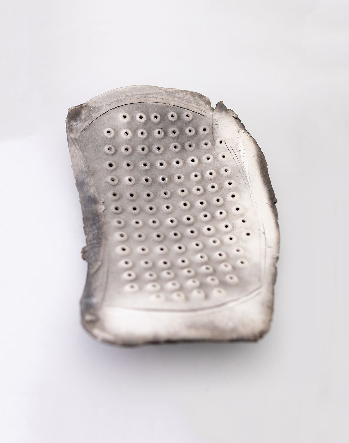 The silver metal grater, featuring a rectangular shape with rounded edges, sits elegantly much like the Two Freeform Raku Platters by John Dunn from RELIC LONDON. Its array of small circular holes and gently worn edges add inviting texture against a plain white background.