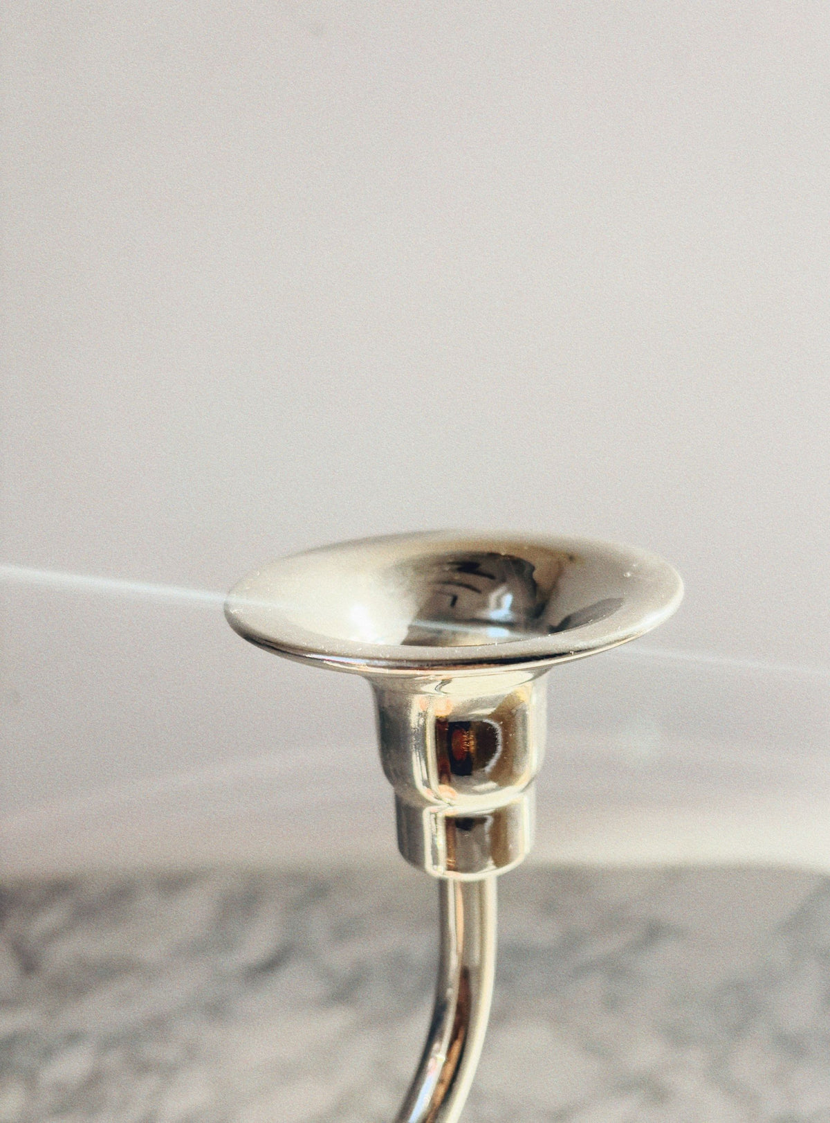A silver Huerto 3 Arm Metal Candleholder gleams against a light backdrop, resembling an art deco piece. Its polished surface reflects light, boasting a luxurious finish that accentuates its smooth contours. The angled photo captures the top and part of its elegant structure.