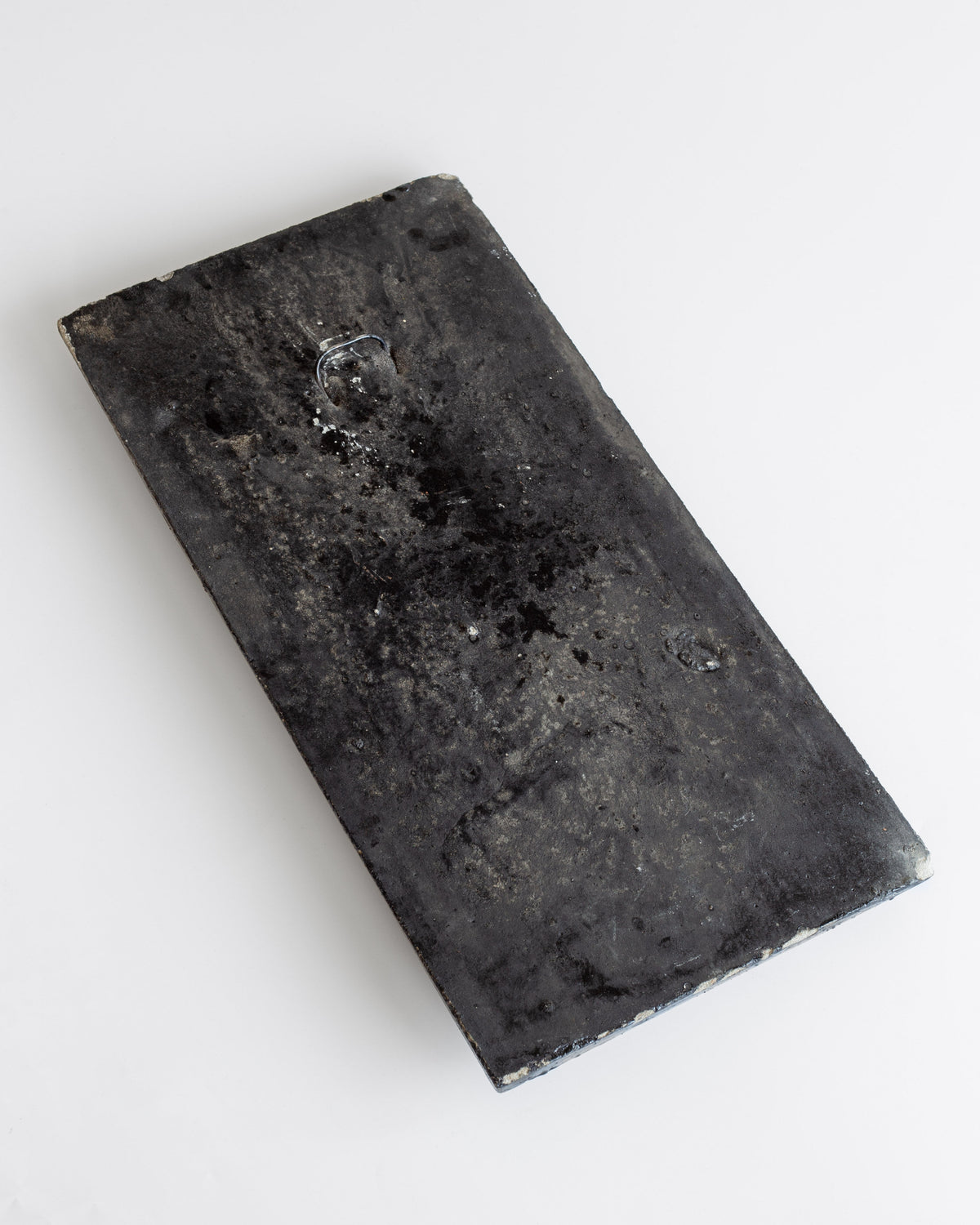 Dark ceramic relief sculpture with water droplets on weathered surface