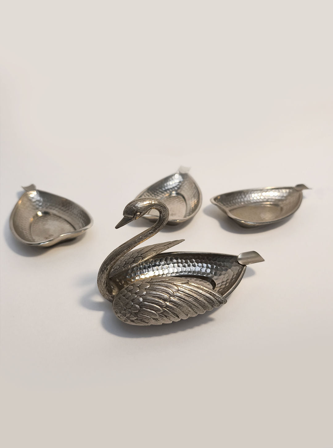 In the foreground is the Swan Ashtray by Les Objoies, featuring detailed feather engravings, accompanied by three smaller leaf-shaped silver bowls ideal for serving or use as unique metal ashtrays.