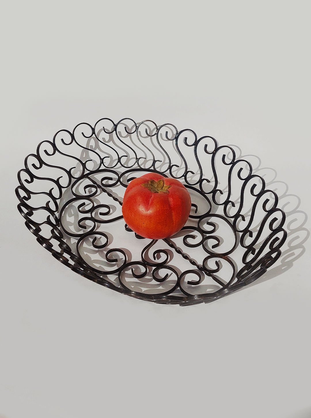 Vintage wrought iron fruit basket with decorative scrollwork holding red tomato