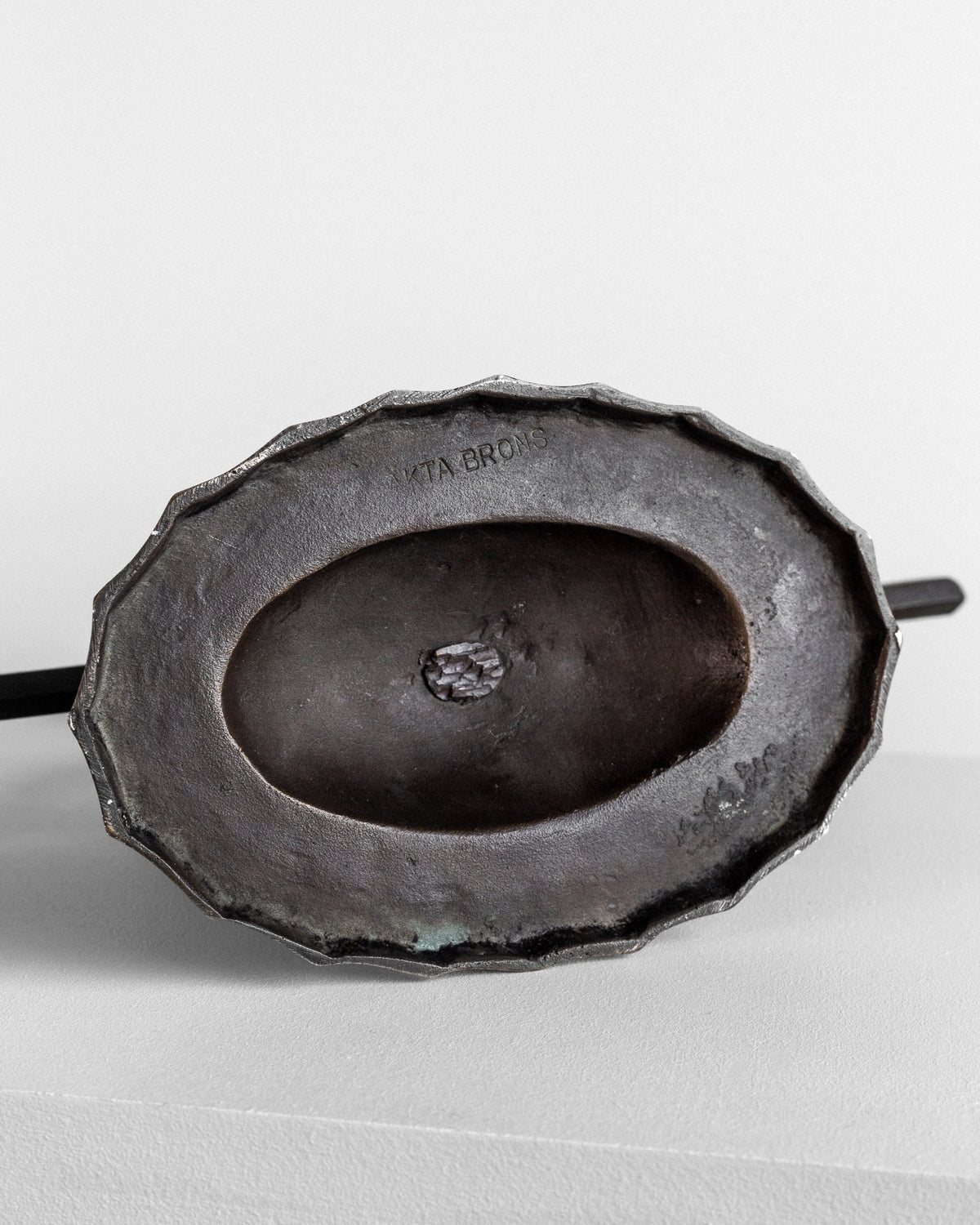 The image showcases a detailed view of the underside of a Spigel Art Deco Bronze Candelabra from the 1930s, featuring an oval indentation and a scalloped outer edge. The engraving "L. VITA BROTHS" is clearly visible on this rustic and aged piece, which rests on a light-colored surface.