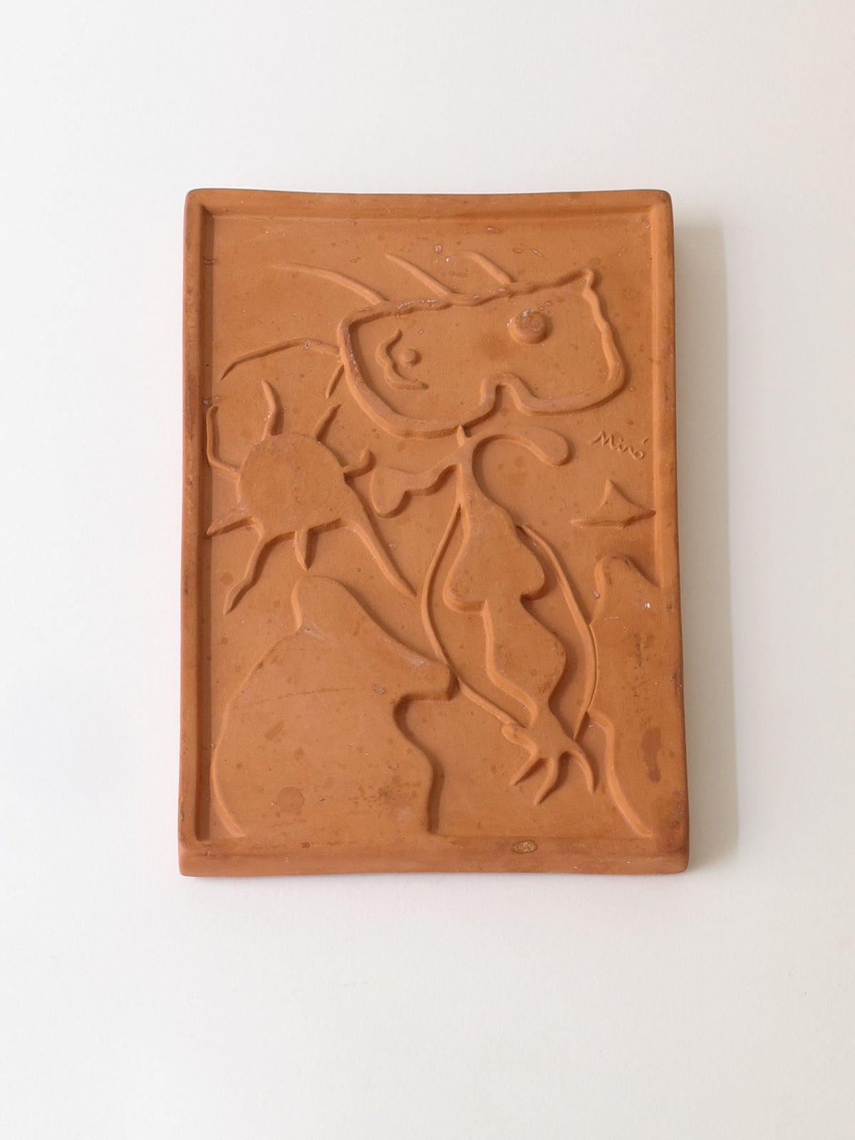 The Terracotta Relief Plaque by Collection apart, signed by Joan Miró (1938), features abstract embossed shapes and lines, a star, and organic forms, with "Miro" engraved on the right side against a plain white background, echoing the Catalan surrealist's style.