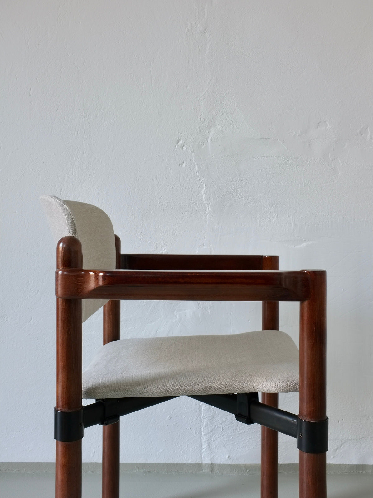 A set of 1970s-style wooden armchairs by Veter Vintage, featuring a light gray fabric seat and backrest, stands against a textured white wall. The chairs, inspired by Fröscher Sitform's design, have armrests and black metal accents connecting the legs.