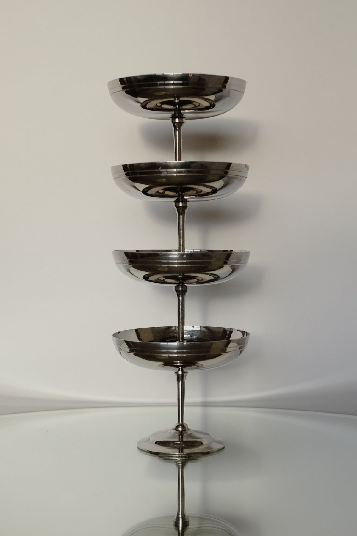 A set of four Ice Coupes from septembre studios is arranged vertically, reflecting on a glossy surface. The simple and uncluttered background enhances the focus on the elegant glassware.