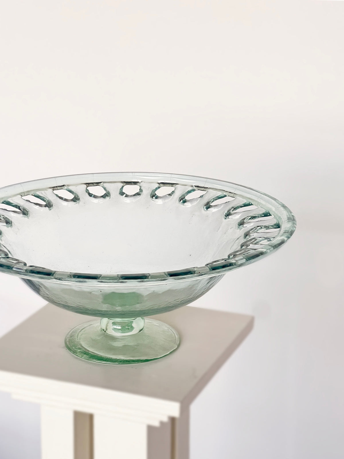 Green glass footed bowl with pierced rim detail on white pedestal