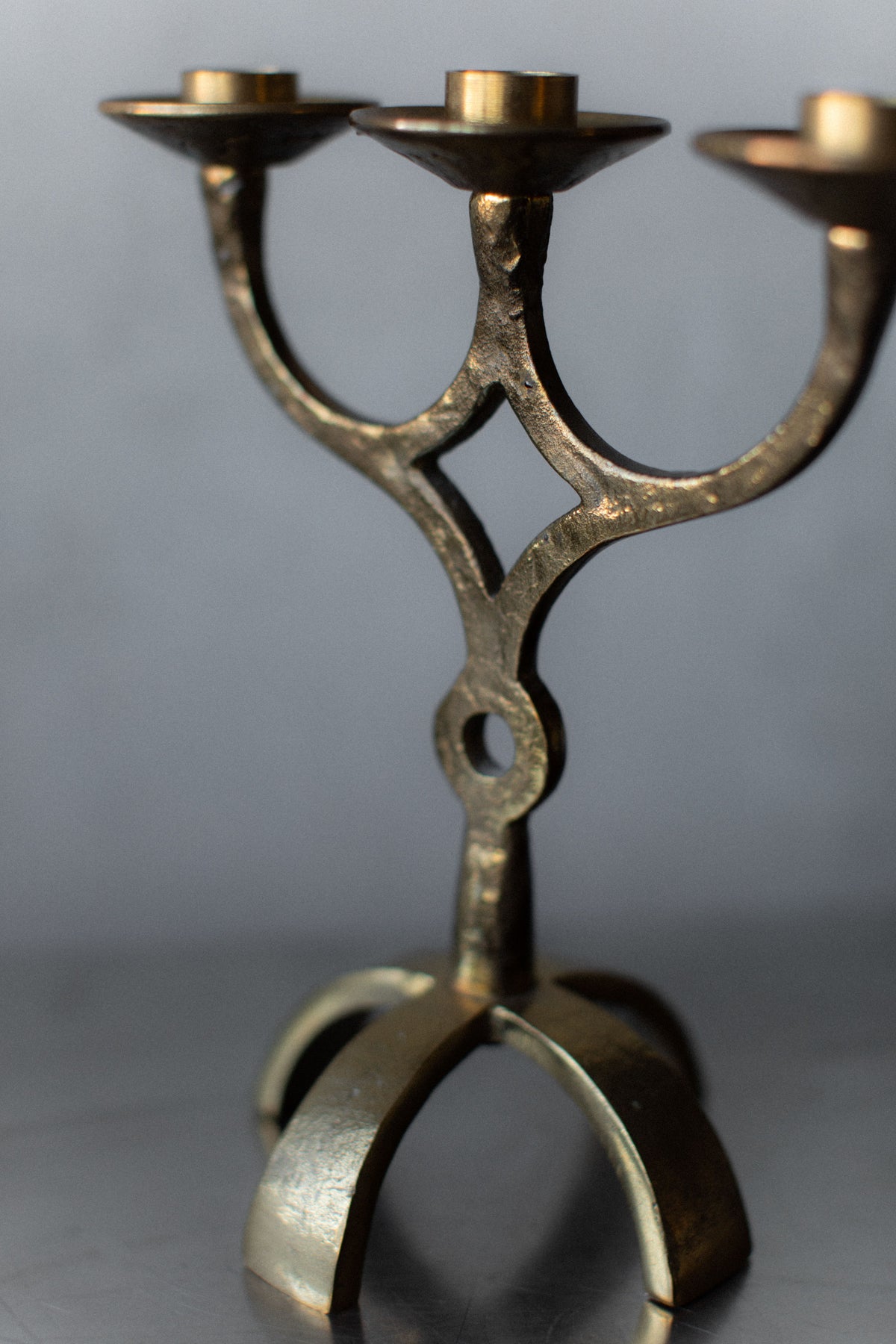 A close-up of the Brutalist Brass Candleholder by Out For Lunch, highlighting its vintage design with three arms and a circular base. The textured brass showcases artisanal craftsmanship against a softly blurred background, emphasizing this striking decorative piece.