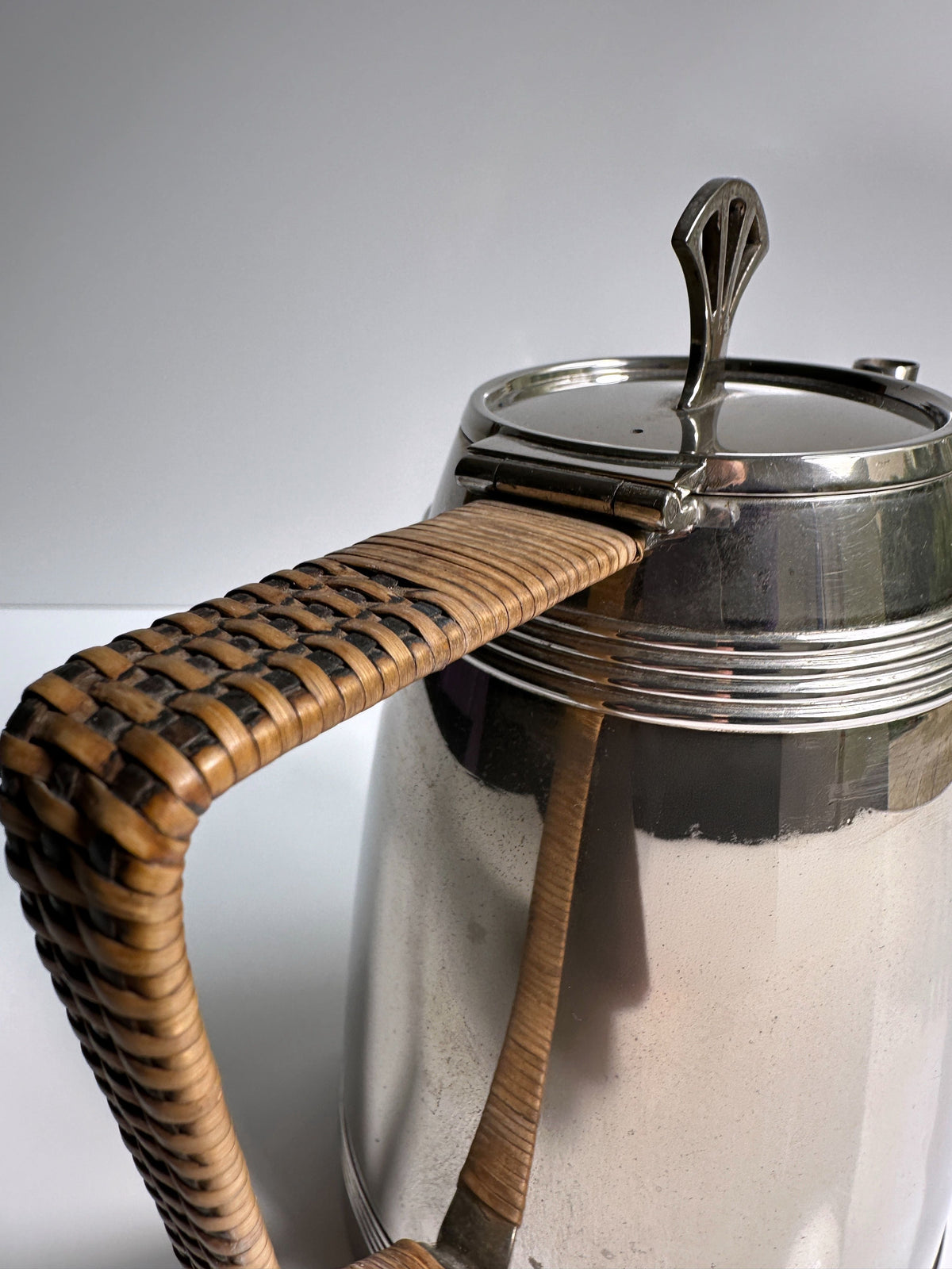 A close-up shows a 1930s Art Deco Silver Coffee Set teapot by Dodo Vintage, featuring a silver body, woven rattan handle, and decorative hinged lid, set against a plain light background.