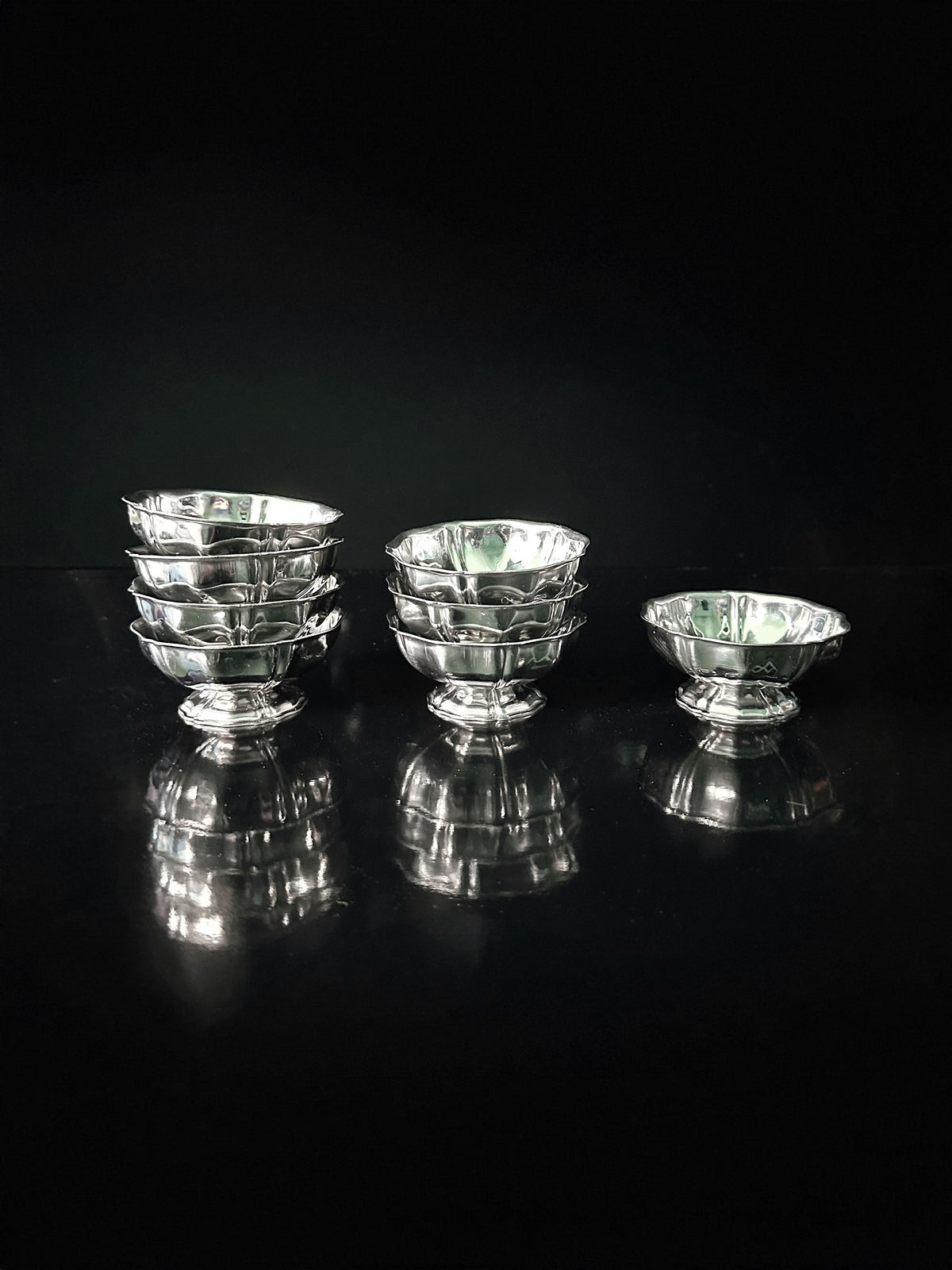 An Italian Stainless Steel Dessert Coupe Set by Dodo Vintage, of varying sizes, arranged artistically against a dark background. The coupes feature intricate designs and cast reflections on the glossy surface, creating a symmetrical display.