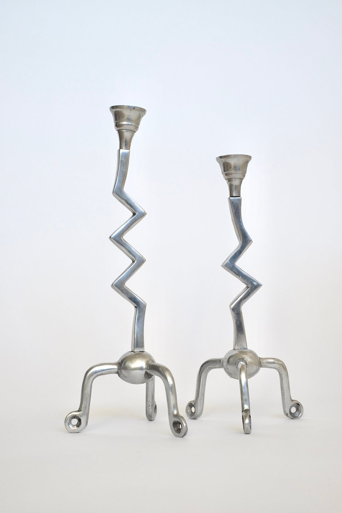 Set against a simple backdrop, the Set of Zigzag Candleholders by septembre studios is a rare treasure. Their silver, artistic design features twisting stems leading to candle holders on three-legged bases, adding a modern touch to any setting.