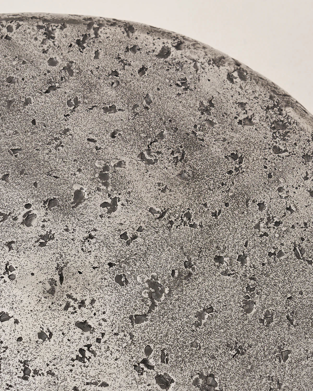 The Crater - Set of 2 by LMNOH features a textured surface similar to rough stone or concrete. Its gray tones and speckled indentations evoke a lunar landscape, creating an intriguing celestial centerpiece for any modern interior.