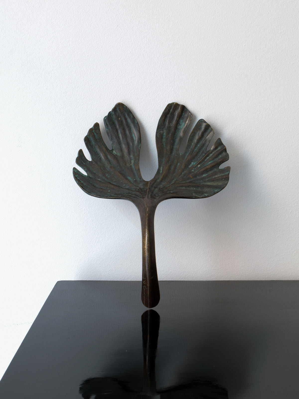 The Bronze Jobin Sculpture by Collection apart, designed to resemble a stylized ginkgo biloba leaf with two broad and textured lobes, is showcased on a glossy black surface against a white background.