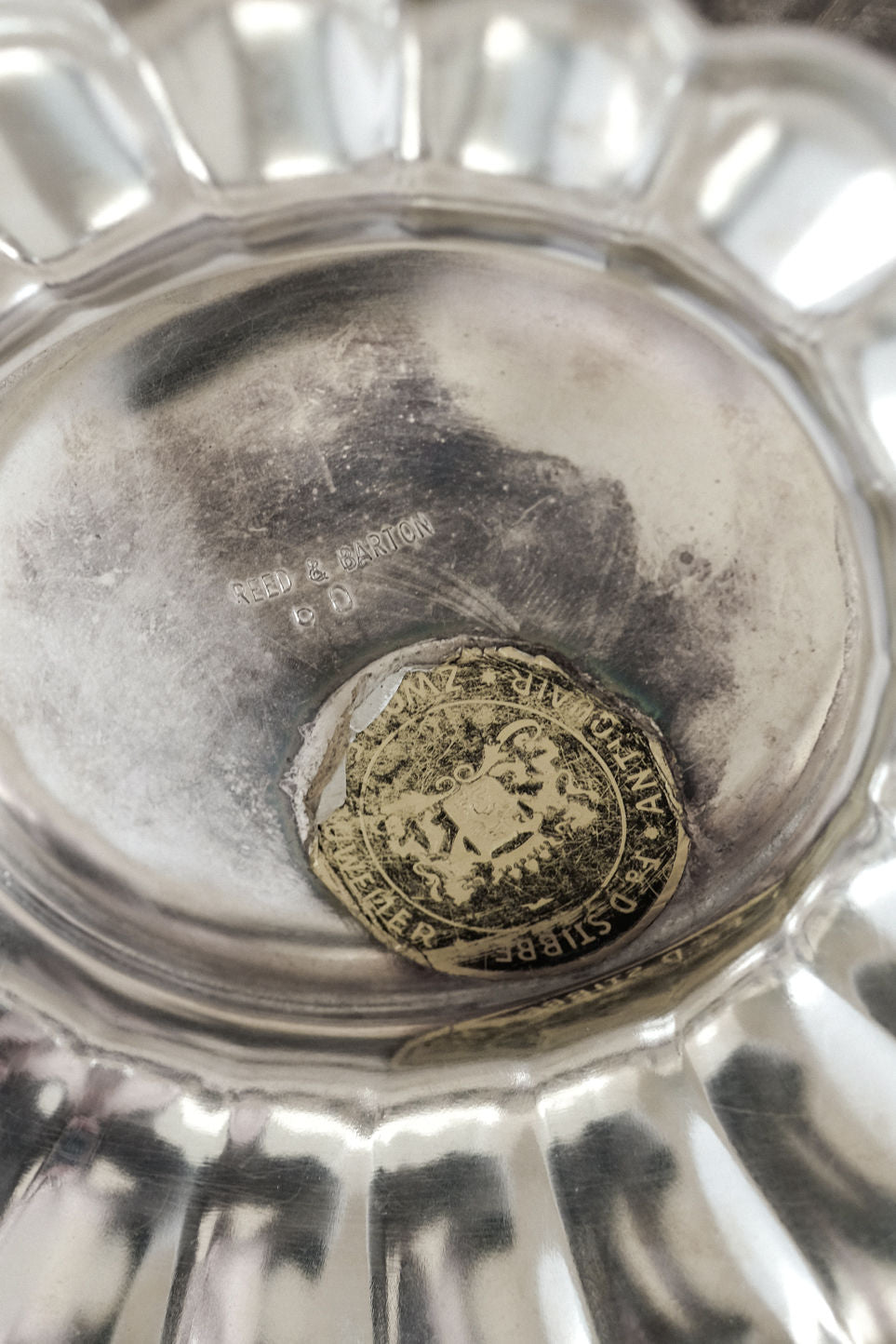 A close-up of the underside of a septembre studios Silverplated Centerpiece shows a faded gold and black sticker and engraved text. The centerpiece features a scalloped edge.