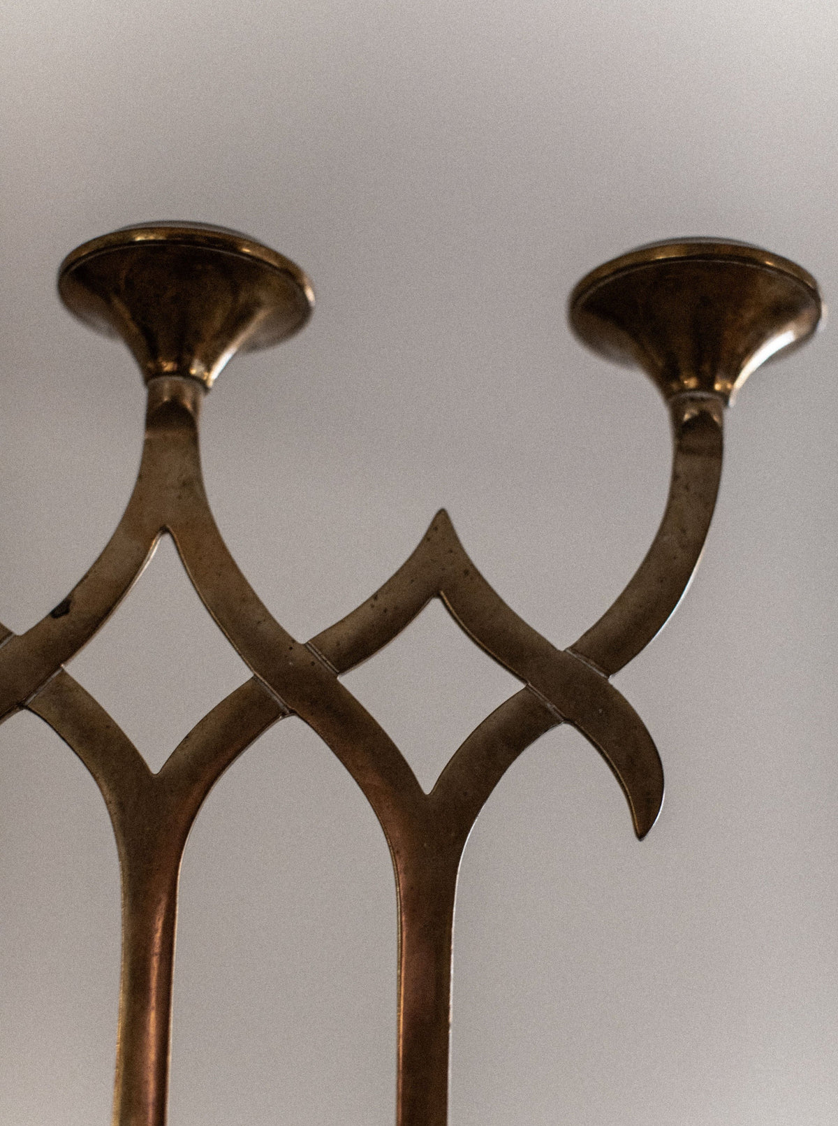 A close-up shot of the "Out For Lunch" Brass Candleholder reveals its vintage charm, showcasing two branches with candle sockets. The design highlights elegant, curved lines forming an intricate pattern, and the brass features a beautifully tarnished, antique finish. This unique home decor piece adds character to any space while the softly blurred background enhances its appeal.
