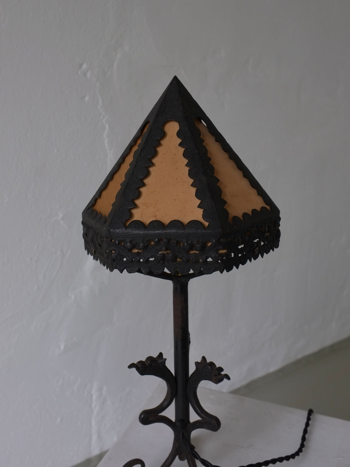 The Veter Vintage Wrought Iron Dragon Table Lamp, Italy 1910s, features dragon details, a triangular scalloped-edge silk shade, and an ornate dark metal base, set against a plain light-colored wall.