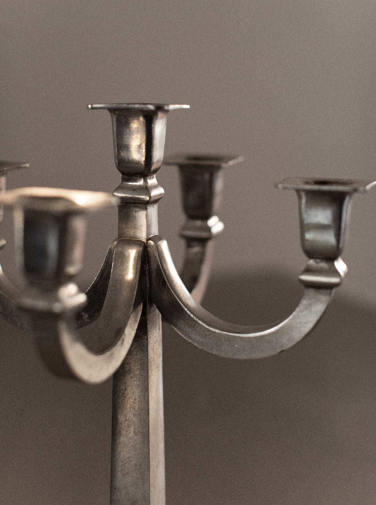 A close-up photo of an elegant silver **Mid-century Candleholder** with five empty candle holders exhibits its vintage, tarnished appearance. The **Out For Lunch Mid-century Candleholder's** distinctive charm adds a touch of sophisticated home decor against a neutral gray background, creating a minimalist and understated look.