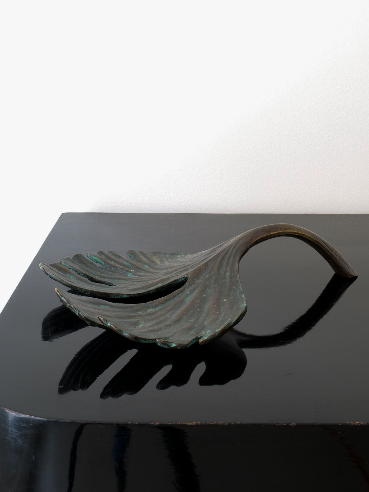 The Bronze Jobin Sculpture by Collection apart, featuring a ribbed textured ginkgo biloba leaf, is beautifully showcased on a glossy black surface. The shadow it casts enhances the depth and elegance of the minimalistic setting.