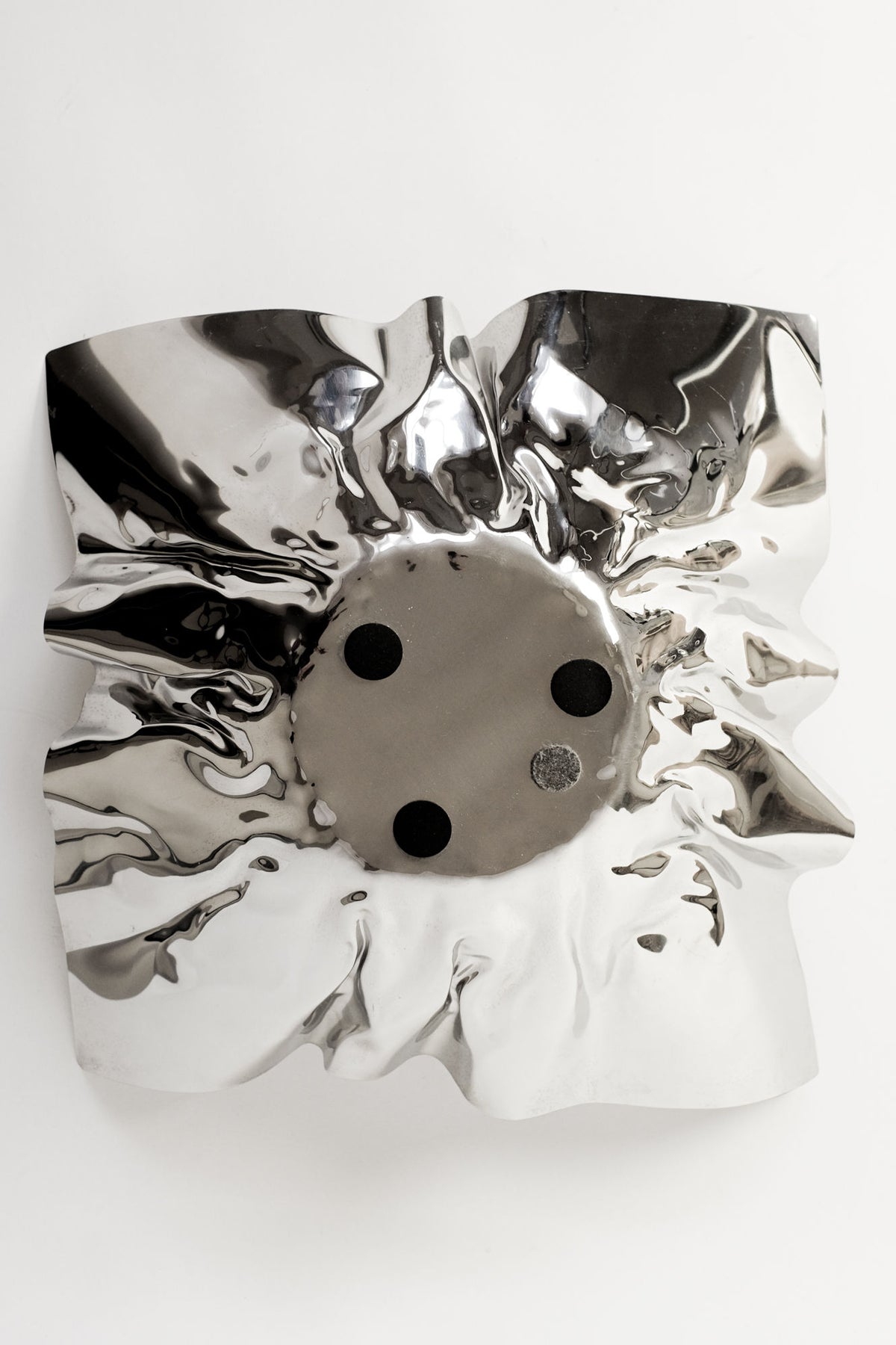 The Extra Large Folded Chrome Bowl by septembre studios is a shiny, reflective silver wall sculpture with a crumpled texture and circular center with three black dots and one gray dot—an eye-catching, vintage-inspired accent for modern interiors. Displayed on white.