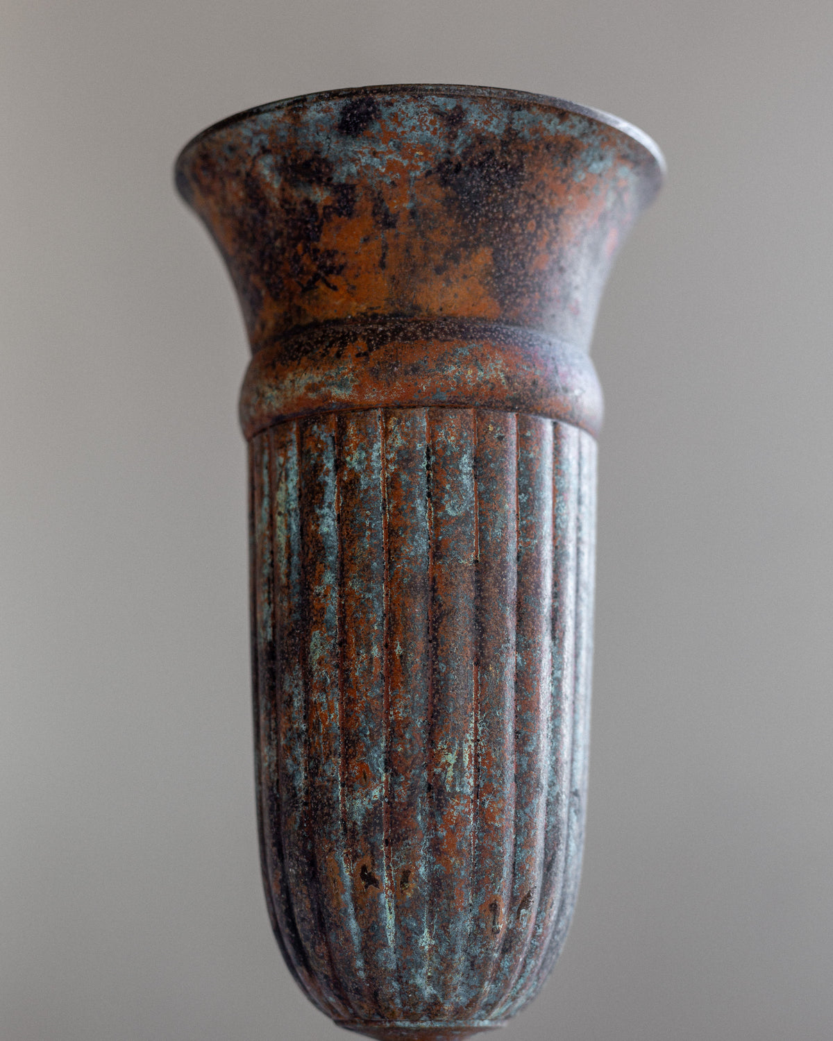A vintage cast iron vase from Spigel, featuring a flared top and vertical ridges, exudes an antique character with its blue-green patina set against a plain gray background.