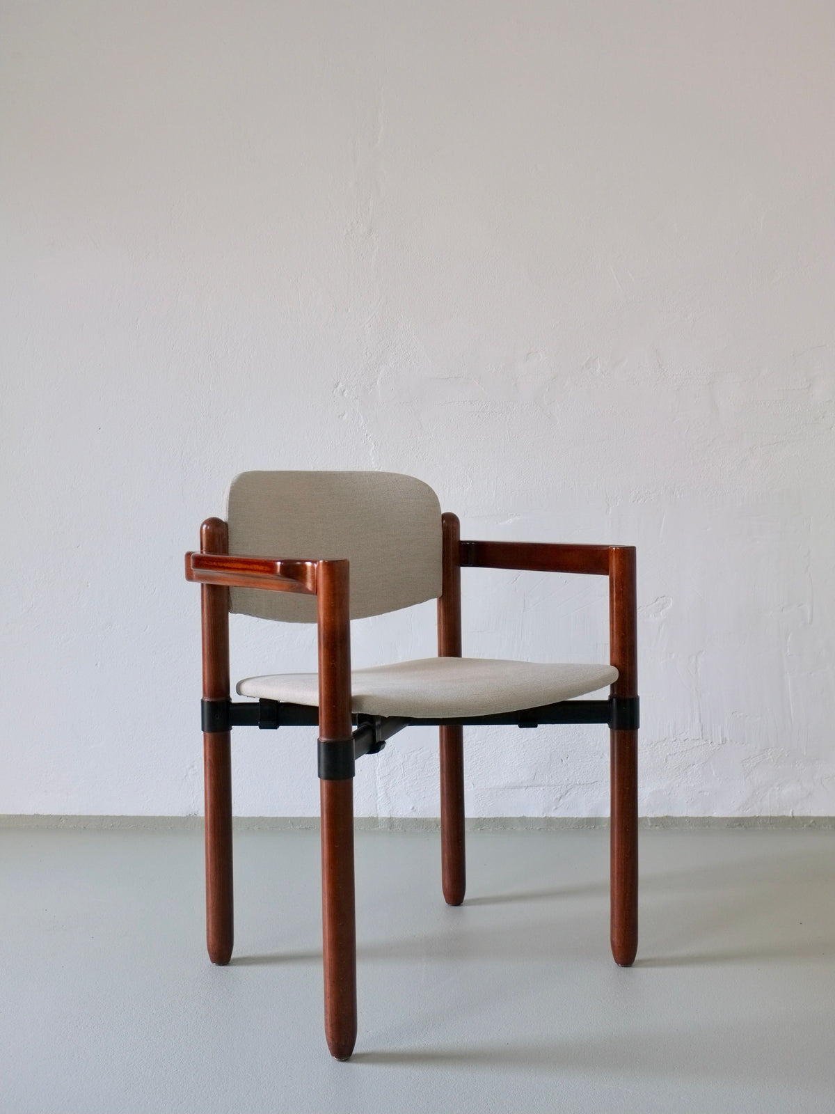 A set of 4 minimalist wooden armchairs by Fröscher Sitform, embodying 1970s design with a light-colored cushioned seat and backrest, rests against a plain light gray wall. Their simple style features vertical and horizontal wooden elements with black metal accents. Available at Veter Vintage.