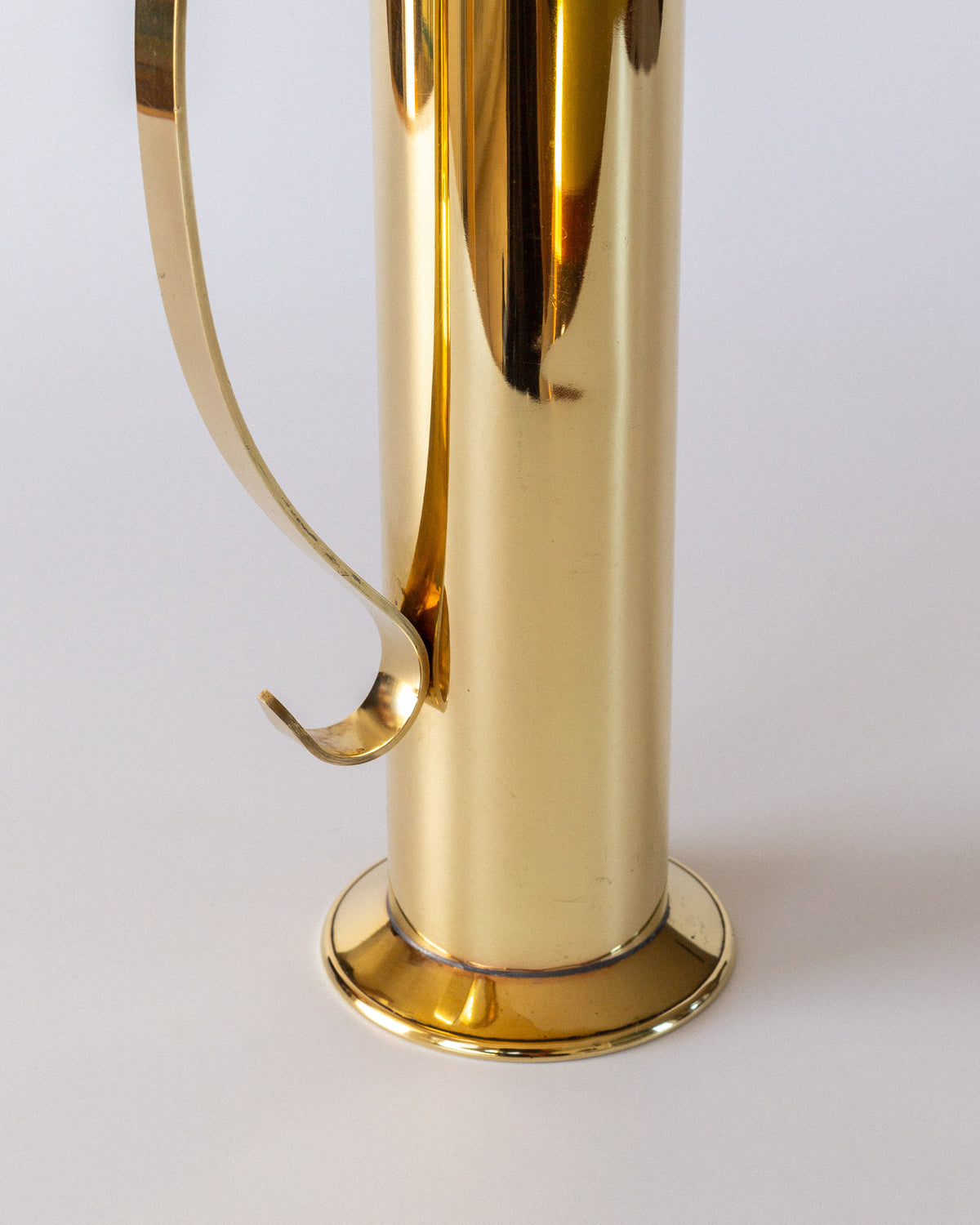 Close-up of the Spigel Large Mid-Century Brass Vase, featuring a shiny gold-tone cylindrical body, curved handle, and round base, displayed against a plain white background.