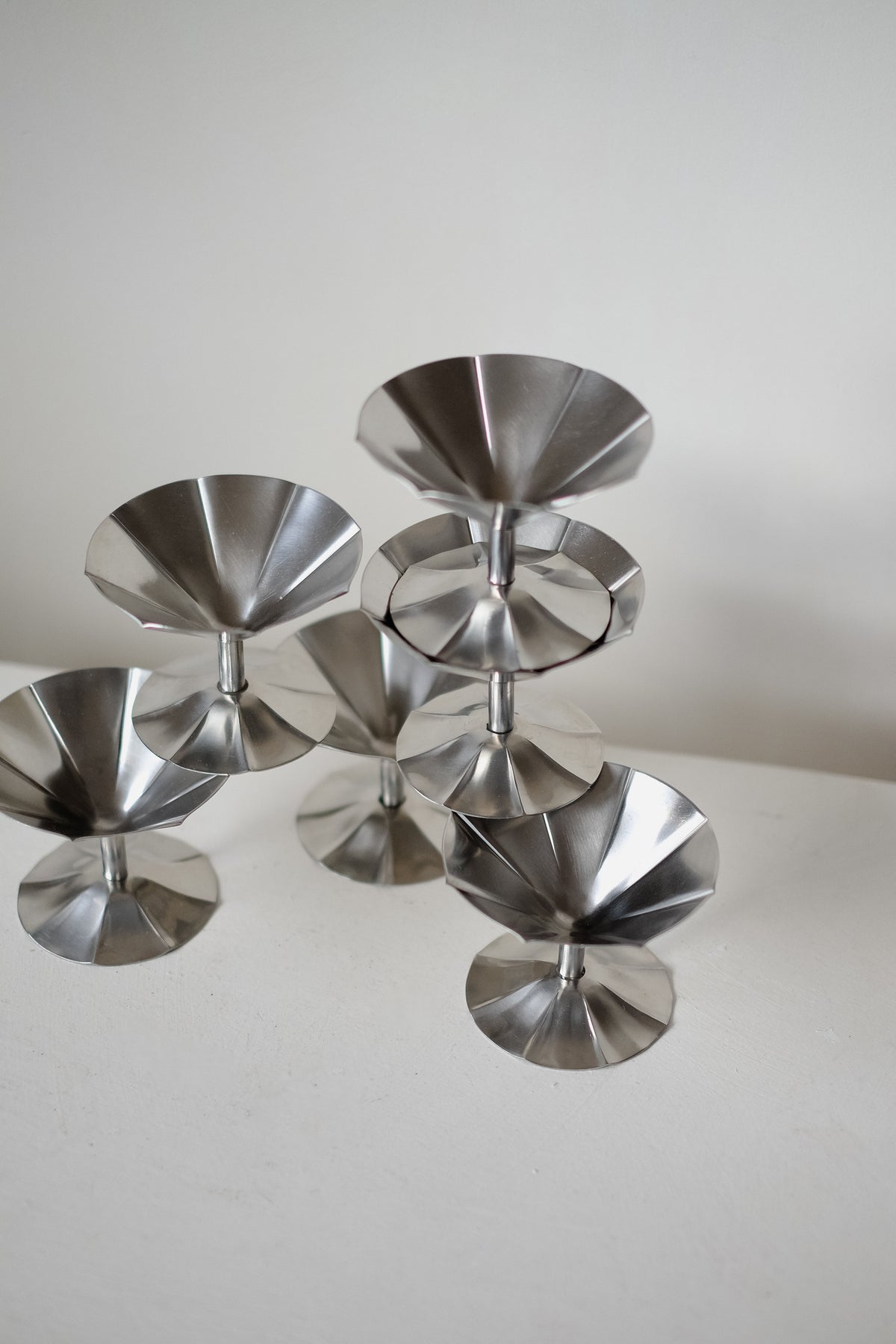 A set of modern, stainless steel ice coupe sculptures by septembre studios is arranged geometrically on a white surface. Each polished, reflective piece exudes a sleek and contemporary vibe, reminiscent of the Sola set design against the simple background.