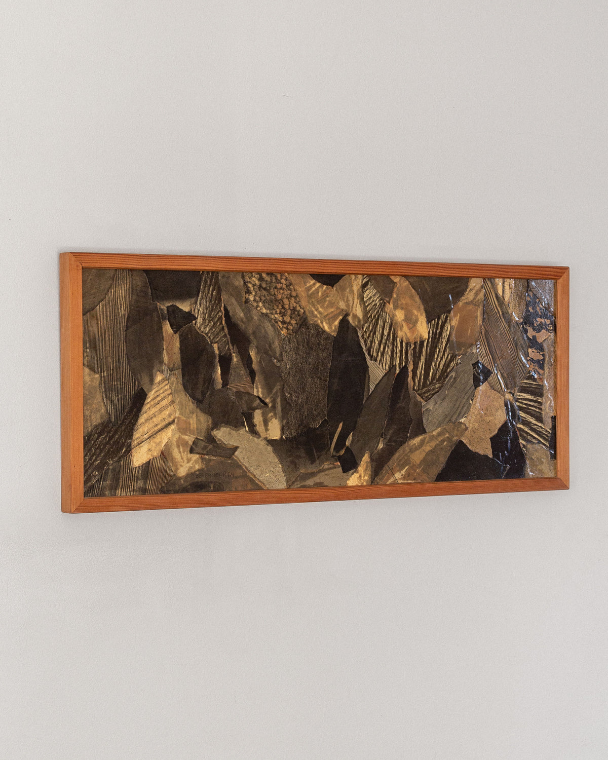 A rectangular wooden frame showcases the "Leaves" collage by Lars Bergander, combining dark, textured rock-like shapes on a light gray wall. This 1960s abstract piece from Sweden embodies depth and movement with mid-century modern Scandinavian art influences. Brand: Spigel.