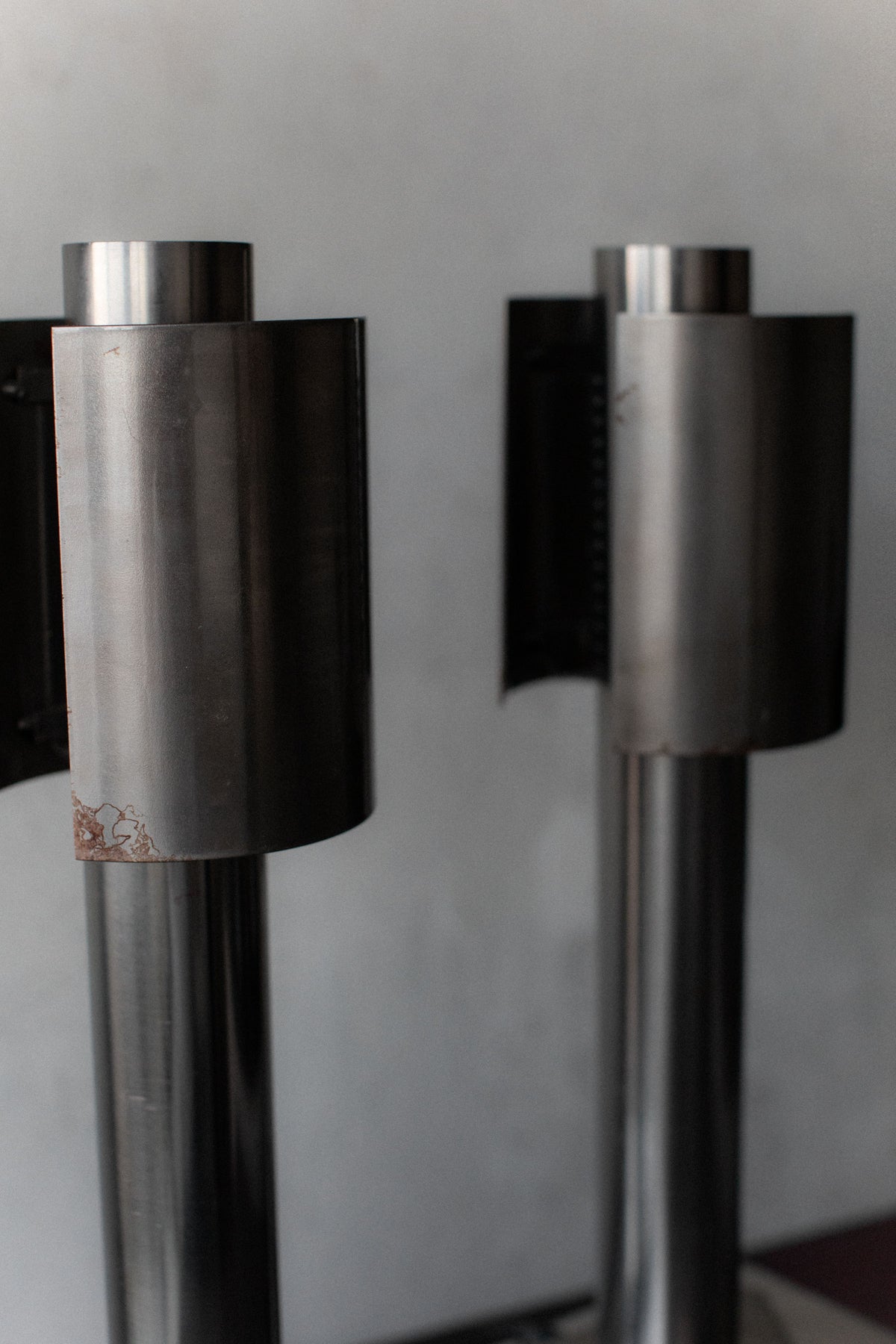 Two 1960's Space Age Lamps from Out For Lunch stand side by side on a plain background. The metallic, cylindrical objects have smooth surfaces with blemishes and a brushed finish, embodying an industrial design that echoes the timeless aesthetic of the space age era.