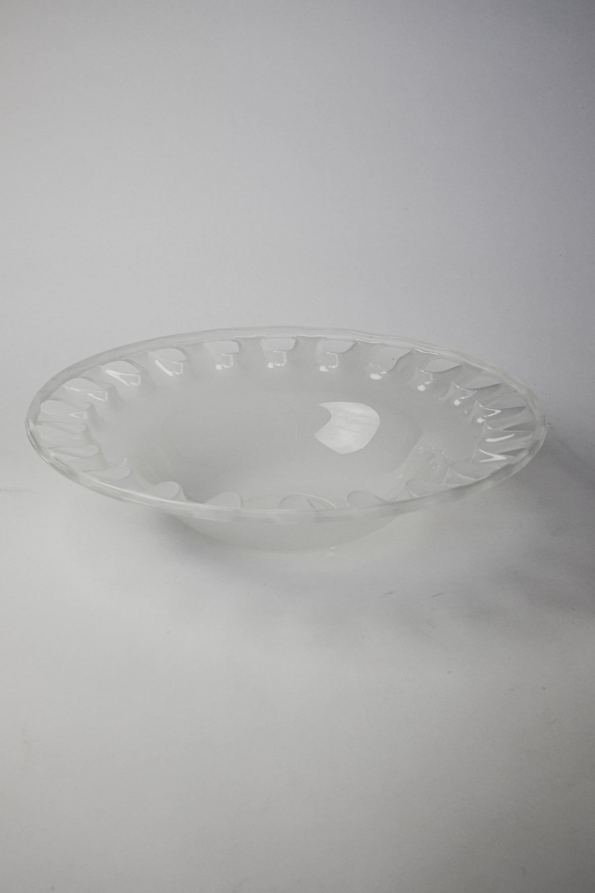 A Large Bowl of Milk Glass by septembre studios rests against a white background. The lighting highlights its smooth surface and scalloped edges, showcasing the glossy, transparent, XL glass's reflective qualities.