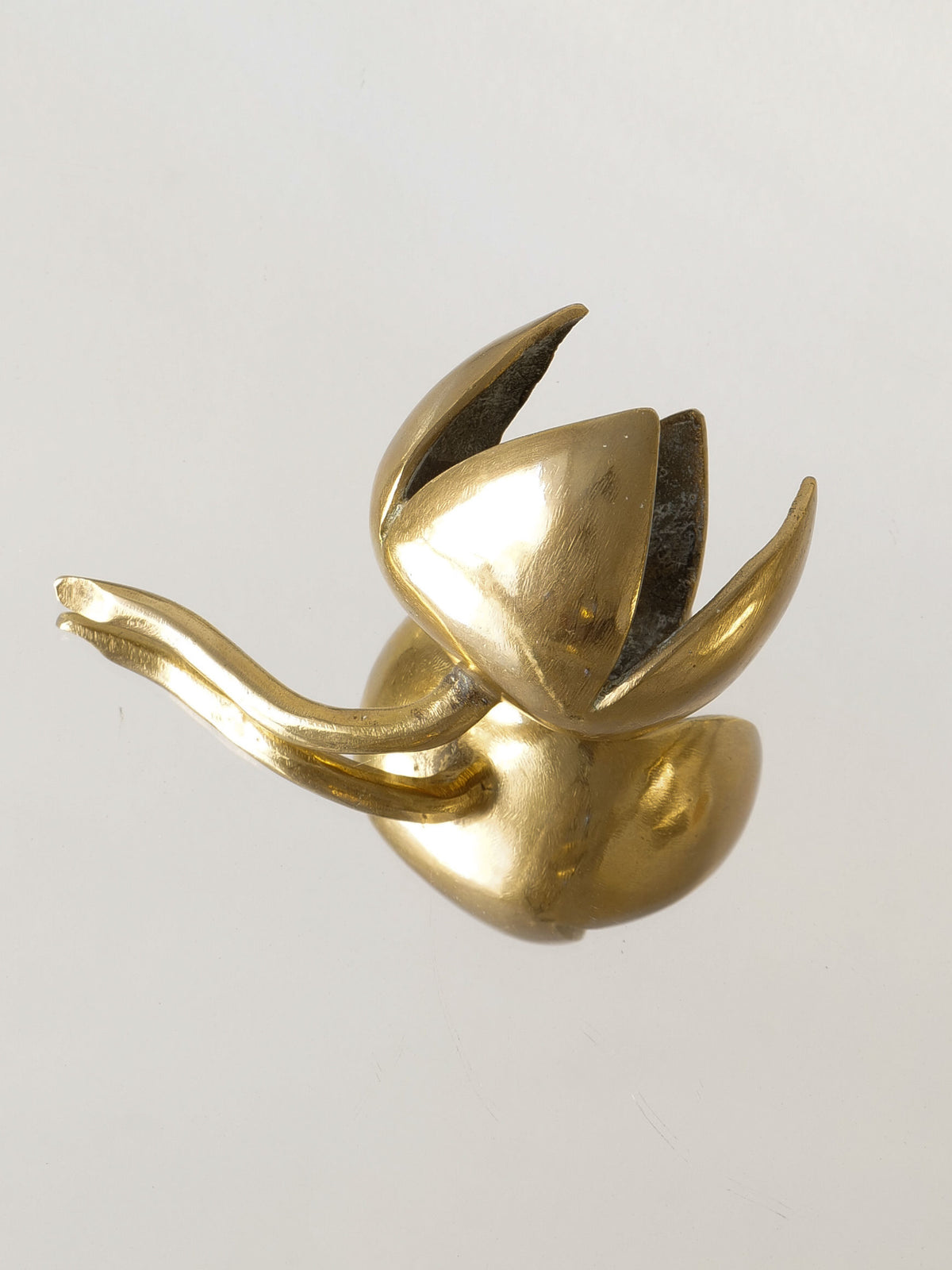 A delicate piece from the Brass Sculpture Collection by Collection apart, this small sculpted object features a stylized flower with a curved stem and open petals, evoking midcentury French design as it rests gracefully on a reflective surface.