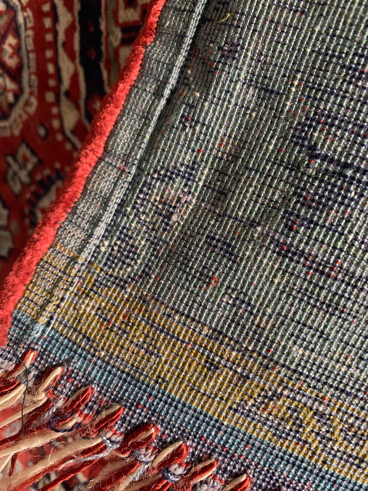 Close-up of the Veter Vintage Silk Oriental Duvet Cover - Rug edge with red trim, detailed threads, and fringe. Features dark blue, yellow, and red patterns; a section of another patterned rug is visible in the background.