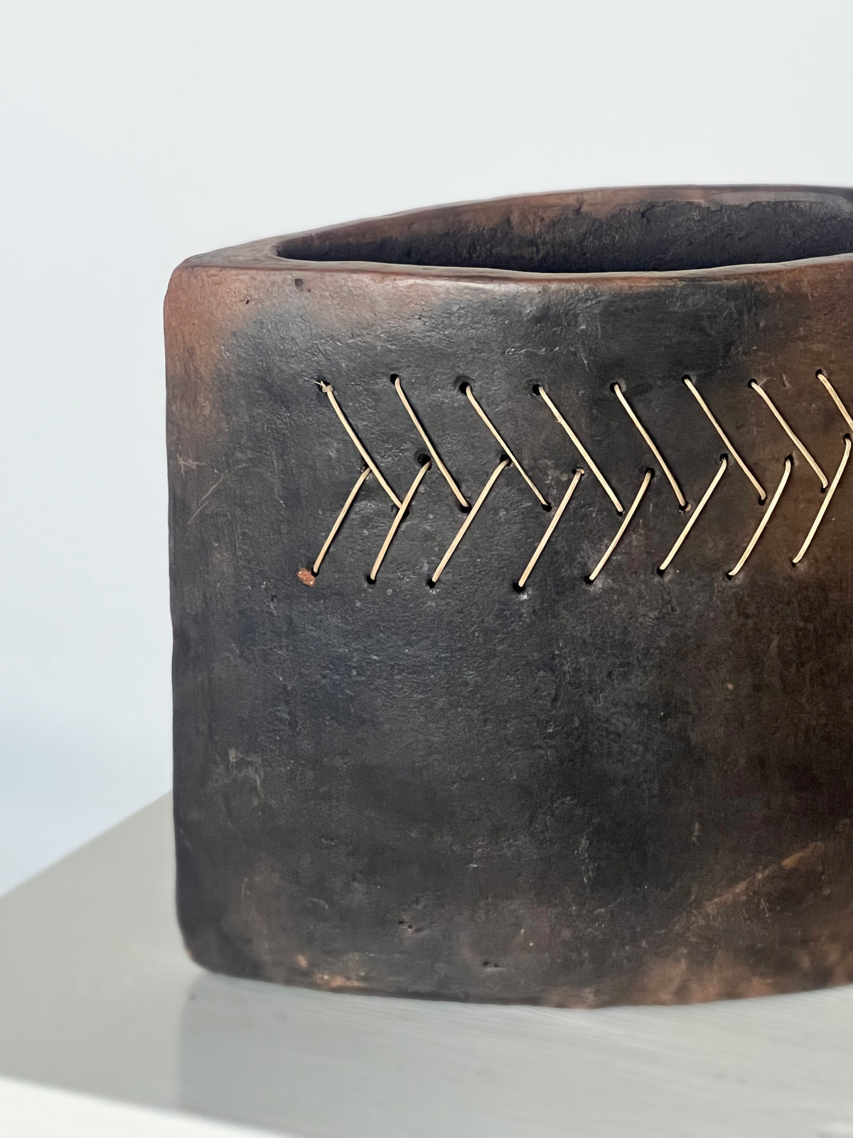 Handwoven brass wire detail on dark terracotta ceramic vase
